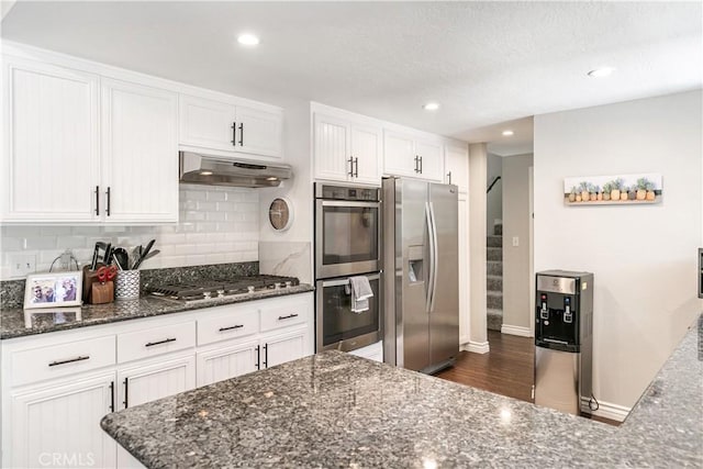 248 Hemlock Dr, Lake Arrowhead, CA 92352 - kitchen featuring appliances with stainless steel finishes, under cabinet range hood, white cabinetry, tasteful backsplash, and dark stone countertops