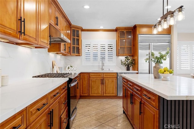 16186 Mount Gist Cir, Fountain Valley, CA 92708 - kitchen featuring gas range oven, built in fridge, under cabinet range hood, ornamental molding, and brown cabinets