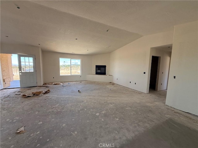 9570 Mescalero Rd, Phelan, CA 92371 - unfurnished living room featuring a textured ceiling, a glass covered fireplace, and lofted ceiling