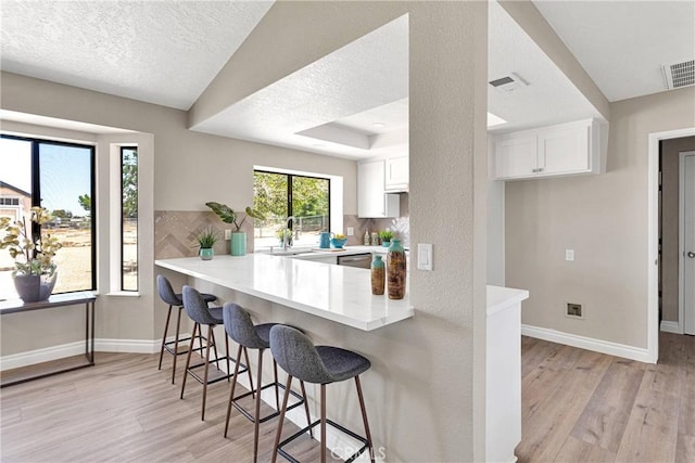 11969 Pinon Ave, Hesperia, CA 92345 - kitchen featuring light wood-type flooring, a kitchen breakfast bar, light countertops, white cabinetry, and a textured ceiling