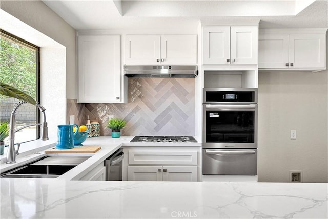 11969 Pinon Ave, Hesperia, CA 92345 - kitchen featuring appliances with stainless steel finishes, a warming drawer, under cabinet range hood, backsplash, and white cabinetry