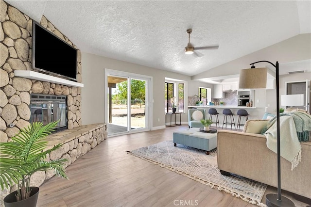 11969 Pinon Ave, Hesperia, CA 92345 - living room featuring ceiling fan, lofted ceiling, light wood-style flooring, a fireplace, and a textured ceiling