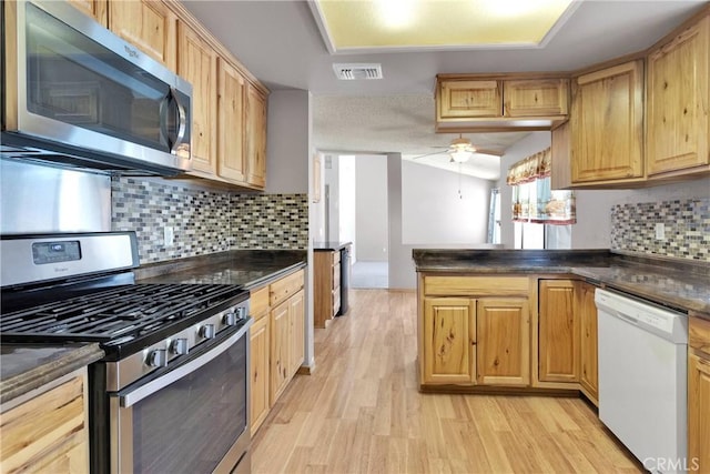 13491 Solitude Cir, Victorville, CA 92392 - kitchen with appliances with stainless steel finishes, dark countertops, a peninsula, light wood-style floors, and decorative backsplash