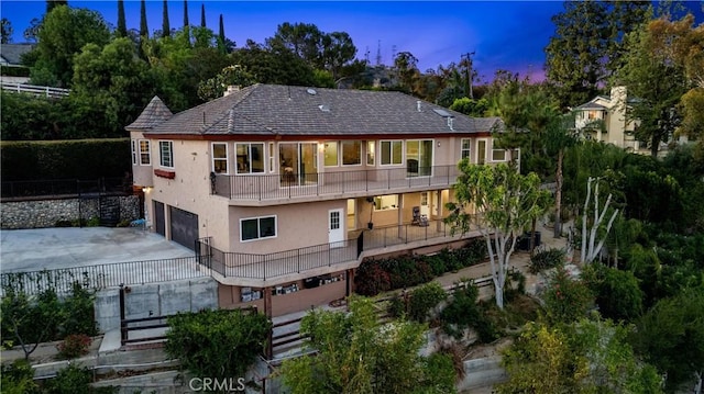 918 Reposado Dr, La Habra Heights, CA 90631 - back of house at dusk featuring a balcony, stucco siding, a garage, concrete driveway, and view of scattered trees