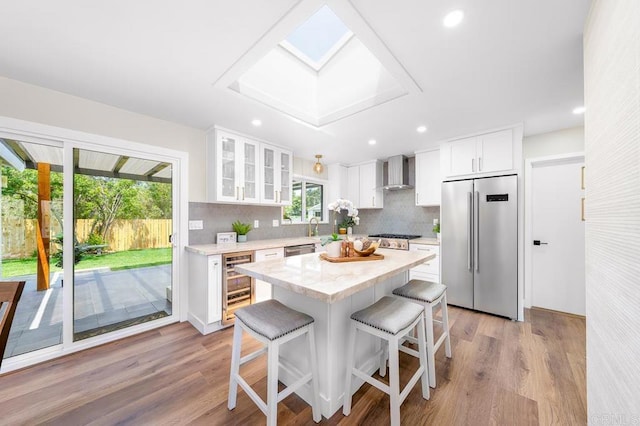 6270 Meadowcrest Dr, La Mesa, CA 91942 - kitchen with stainless steel appliances, wall chimney range hood, beverage cooler, a kitchen breakfast bar, and light wood finished floors