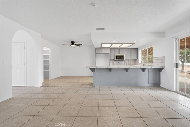 9191 White Rd, Phelan, CA 92371 - kitchen with a peninsula, tile counters, decorative backsplash, a kitchen breakfast bar, and a textured ceiling