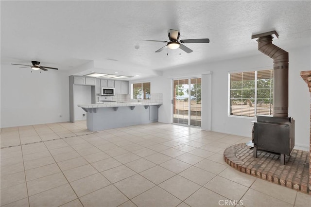 9191 White Rd, Phelan, CA 92371 - unfurnished living room with ceiling fan, a wood stove, and light tile patterned floors