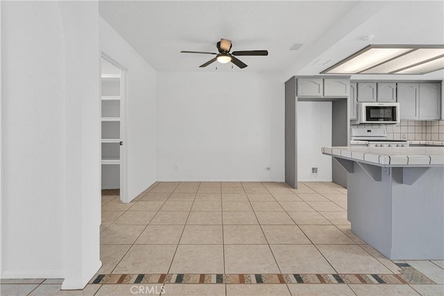 9191 White Rd, Phelan, CA 92371 - kitchen featuring white microwave, tile countertops, stove, and gray cabinetry