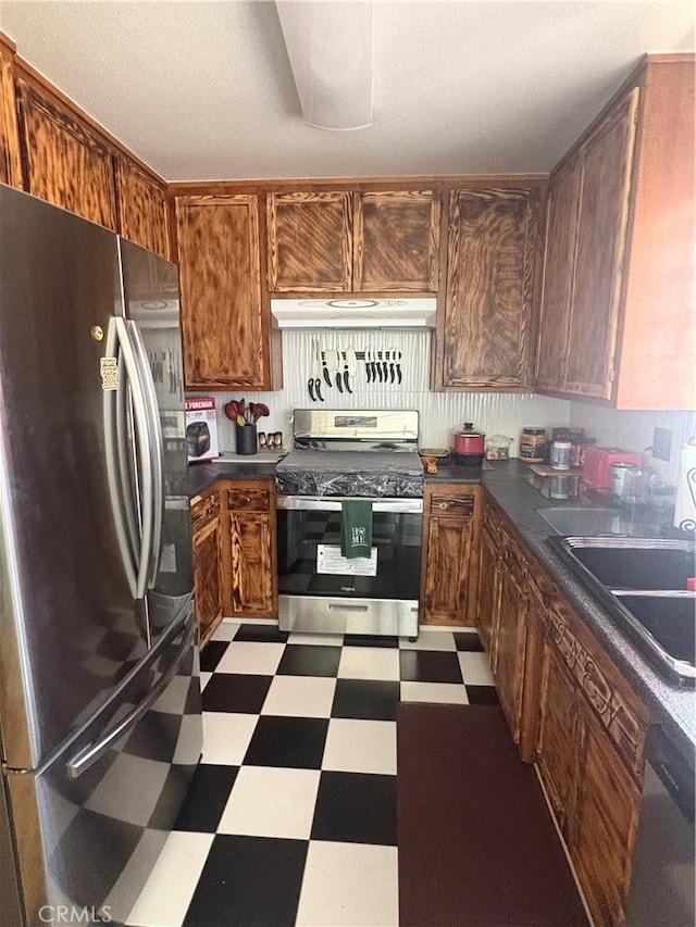 7103 Hanford Ave, Yucca Valley, CA 92284 - kitchen featuring appliances with stainless steel finishes, tile patterned floors, under cabinet range hood, dark countertops, and brown cabinetry