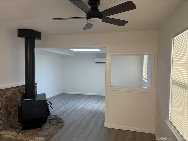 2023 Jewell Ln, Redding, CA 96001 - unfurnished living room featuring a wood stove, an AC wall unit, wood finished floors, ceiling fan, and healthy amount of natural light