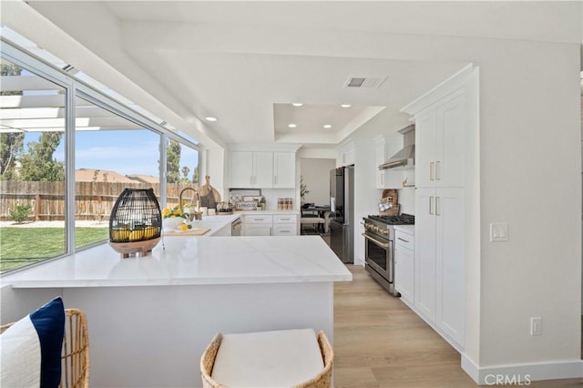 2143 Westminster Dr, Palmdale, CA 93550 - kitchen featuring appliances with stainless steel finishes, light wood finished floors, a peninsula, wall chimney exhaust hood, and white cabinetry