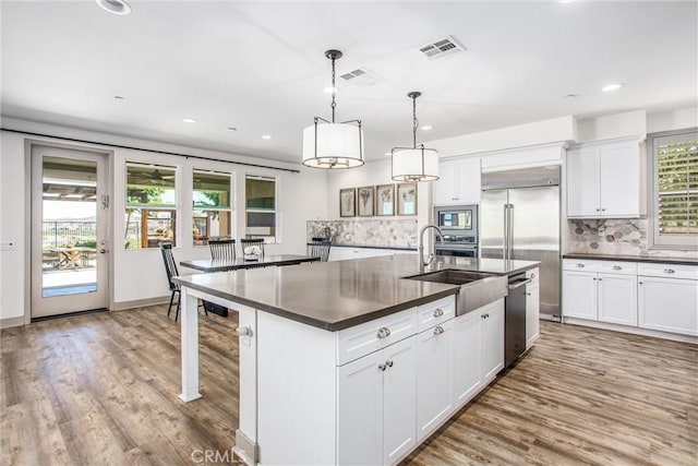 13438 Ambrosia Ct, Riverside, CA 92503 - kitchen with dark countertops, built in appliances, a kitchen island with sink, backsplash, and wood finished floors