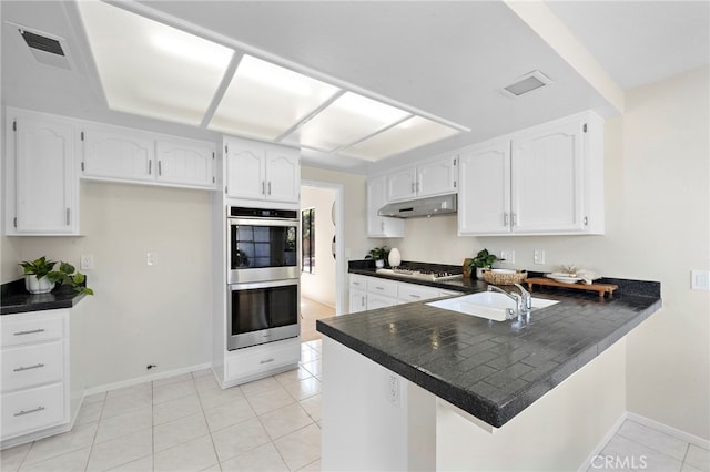 1061 Regis Way, Tustin, CA 92780 - kitchen with under cabinet range hood, dark countertops, appliances with stainless steel finishes, a peninsula, and white cabinets