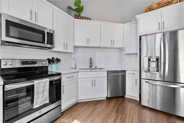 222 N Singingwood St Unit 9, Orange, CA 92869 - kitchen featuring appliances with stainless steel finishes, light countertops, white cabinetry, tasteful backsplash, and light wood finished floors