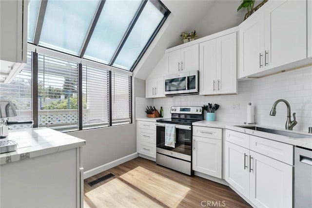 222 N Singingwood St Unit 9, Orange, CA 92869 - kitchen with appliances with stainless steel finishes, vaulted ceiling, backsplash, white cabinets, and light wood-style flooring