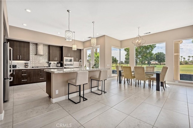 56720 Jack Nicklaus Blvd, La Quinta, CA 92253 - kitchen with appliances with stainless steel finishes, dark brown cabinets, a kitchen breakfast bar, backsplash, and wall chimney range hood
