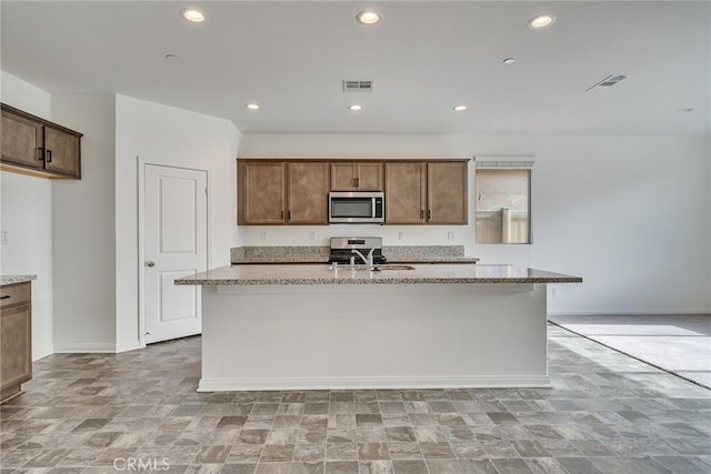 29601 Tulipwood St, Menifee, CA 92584 - kitchen with stainless steel microwave, a kitchen island with sink, stone finish floors, light stone counters, and recessed lighting