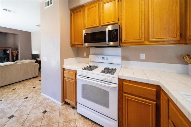 29767 Ascella Ln, Murrieta, CA 92563 - kitchen with gas range gas stove, stainless steel microwave, tile counters, light tile patterned flooring, and brown cabinetry