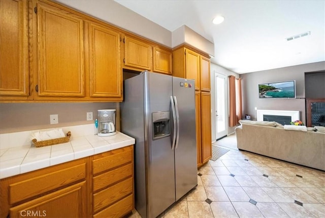 29767 Ascella Ln, Murrieta, CA 92563 - kitchen featuring stainless steel fridge with ice dispenser, tile countertops, open floor plan, brown cabinetry, and a fireplace