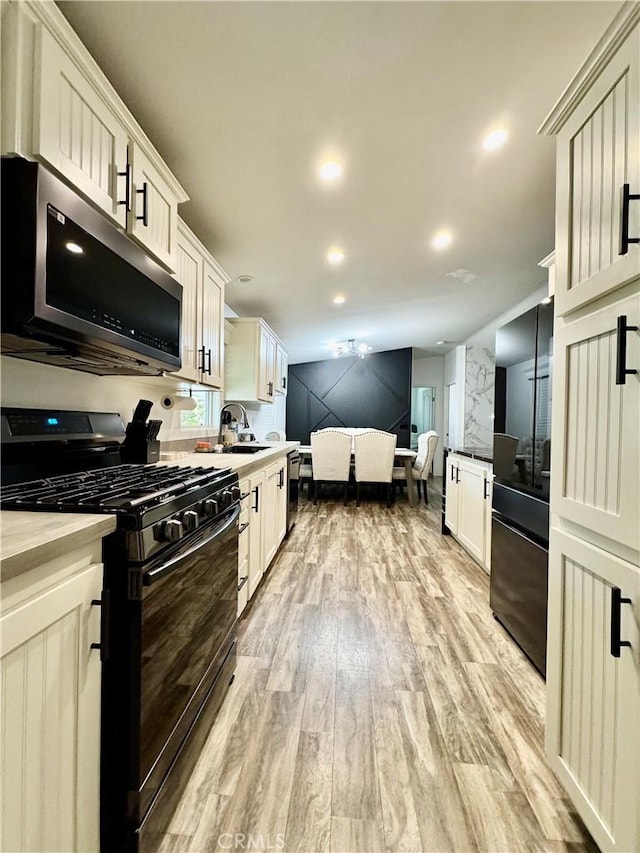 2851 S La Cadena Dr Unit 125, Colton, CA 92324 - kitchen with black range with gas cooktop, stainless steel microwave, freestanding refrigerator, light wood-type flooring, and light countertops