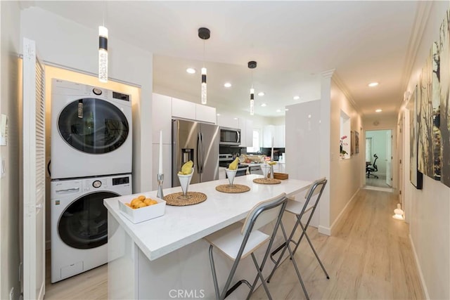 645 N Gramercy Pl, Los Angeles, CA 90004 - kitchen with appliances with stainless steel finishes, estacked washer and dryer, white cabinetry, light wood-style floors, and a breakfast bar
