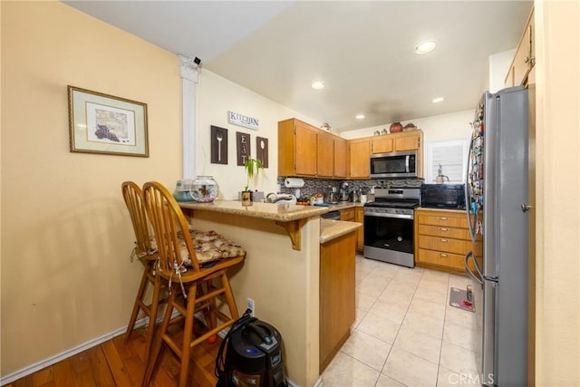 23220 Colony Park Dr, Carson, CA 90745 - kitchen featuring stainless steel appliances, a peninsula, brown cabinetry, backsplash, and a breakfast bar