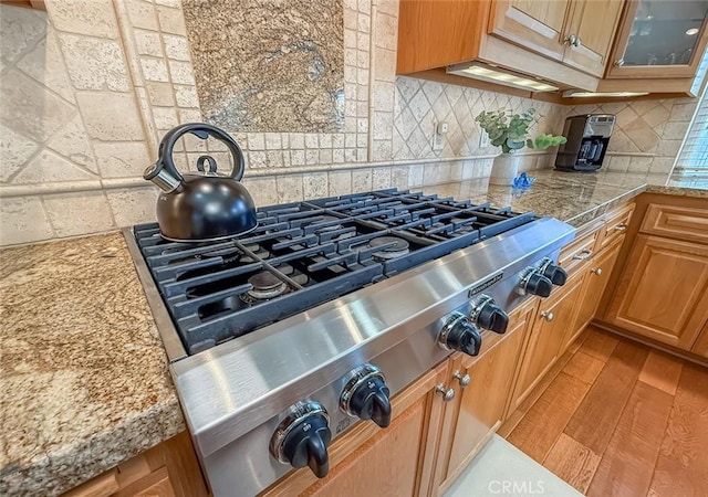 10424 Gloria Ave, Granada Hills, CA 91344 - kitchen view of tasteful backsplash, glass insert cabinets, light stone countertops, light wood-type flooring, and stainless steel gas stovetop
