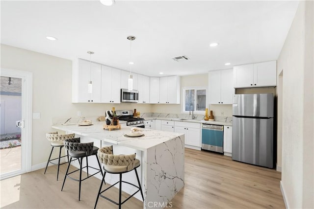 3876 Olmsted Ave, Los Angeles, CA 90008 - kitchen featuring appliances with stainless steel finishes, a peninsula, light stone counters, a kitchen breakfast bar, and light wood-style floors