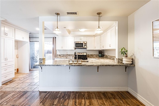 1209 E 1st St, Tustin, CA 92780 - kitchen featuring stainless steel appliances, a peninsula, light stone countertops, white cabinetry, and a kitchen bar