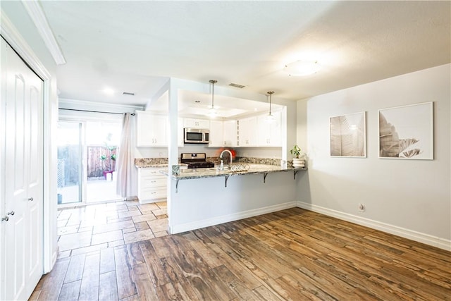 1209 E 1st St, Tustin, CA 92780 - kitchen with appliances with stainless steel finishes, a peninsula, hardwood / wood-style floors, a breakfast bar, and white cabinetry