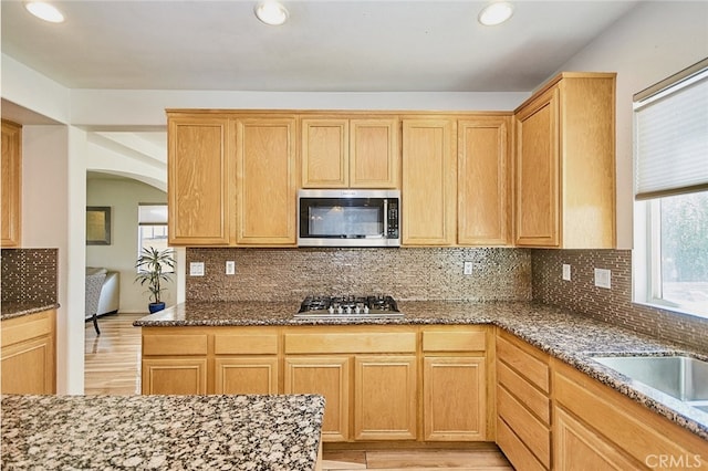 13637 Aspen Leaf Ln, Eastvale, CA 92880 - kitchen with stainless steel appliances, dark stone countertops, arched walkways, light wood-style floors, and recessed lighting