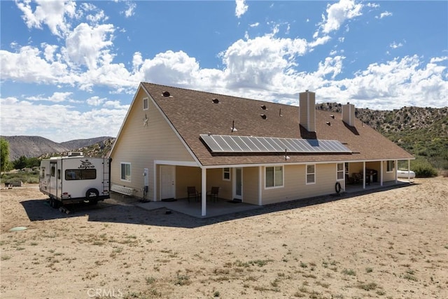 5935 Monte Vista Rd, Phelan, CA 92371 - rear view of house featuring a mountain view, a chimney, roof mounted solar panels, and a patio