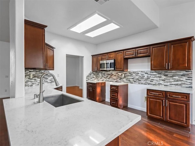 37453 56th St E, Palmdale, CA 93552 - kitchen with stainless steel microwave, light stone counters, dark wood-style flooring, backsplash, and a peninsula