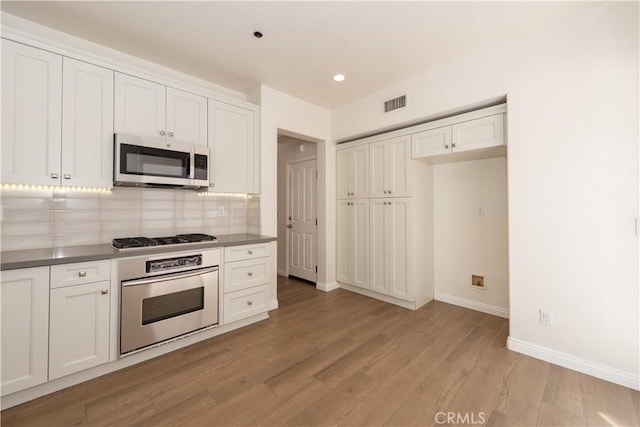 23 Bower Tree, Irvine, CA 92603 - kitchen with appliances with stainless steel finishes, light wood-style flooring, white cabinetry, tasteful backsplash, and dark countertops