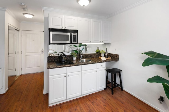 1021 Scott St Unit 130, Point Loma, CA 92106 - kitchen featuring stainless steel microwave, dark wood-type flooring, white cabinetry, ornamental molding, and dark stone counters