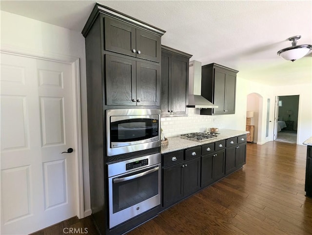 1785 Durham Dayton, Durham, CA 95938 - kitchen featuring stainless steel appliances, wall chimney range hood, decorative backsplash, arched walkways, and dark wood finished floors
