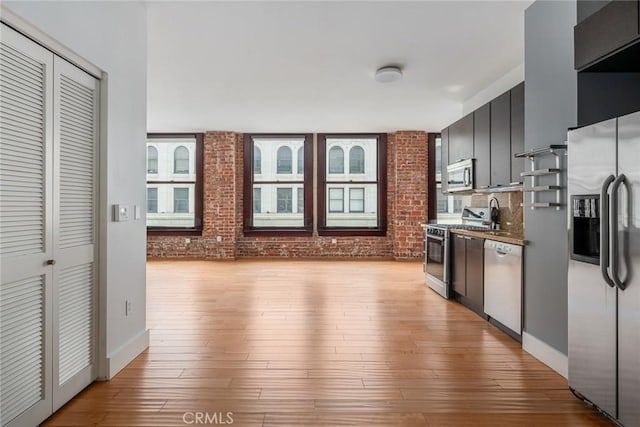 460 S Spring St Unit 1013, Los Angeles, CA 90013 - kitchen with stainless steel appliances, light wood-type flooring, backsplash, brick wall, and dark cabinets
