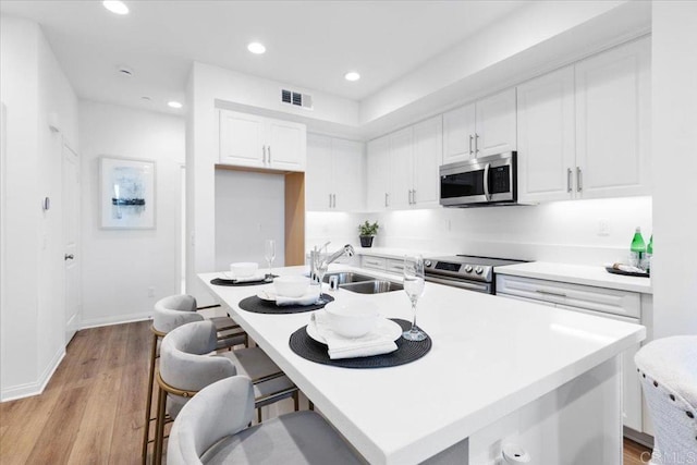 314 El Cajon Blvd, El Cajon, CA 92020 - kitchen with stainless steel appliances, white cabinets, a breakfast bar, light countertops, and light wood-style floors