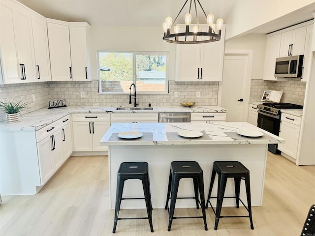 7118 Stanford Ave, La Mesa, CA 91942 - kitchen with appliances with stainless steel finishes, a kitchen breakfast bar, light wood-style floors, decorative backsplash, and white cabinets