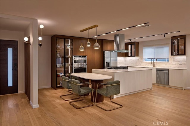 26144 Kenrose Cir, Calabasas, CA 91302 - kitchen with appliances with stainless steel finishes, island range hood, tasteful backsplash, light wood-type flooring, and glass insert cabinets
