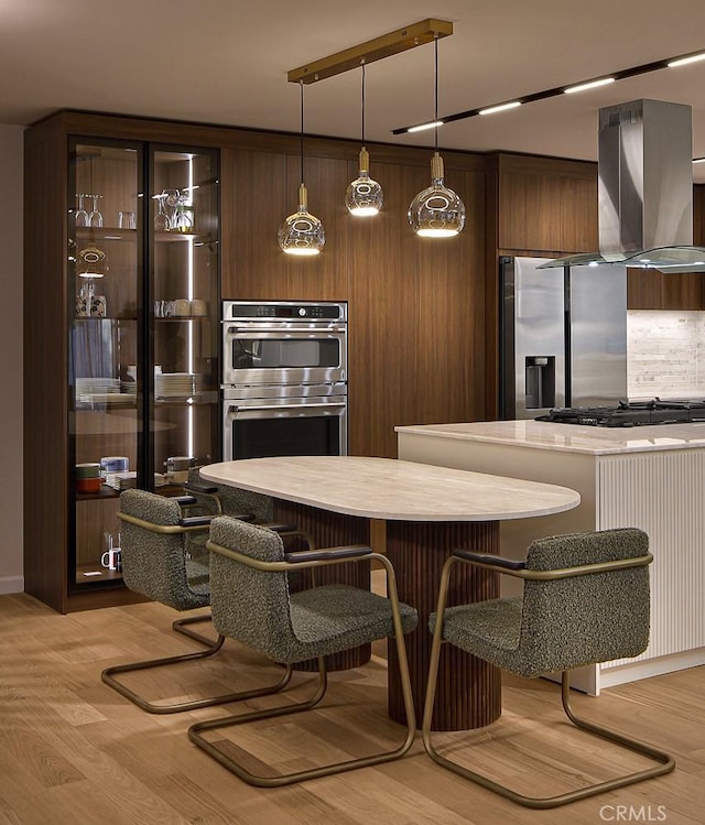 26144 Kenrose Cir, Calabasas, CA 91302 - kitchen featuring wall chimney exhaust hood, stainless steel appliances, light wood finished floors, decorative light fixtures, and a breakfast bar area
