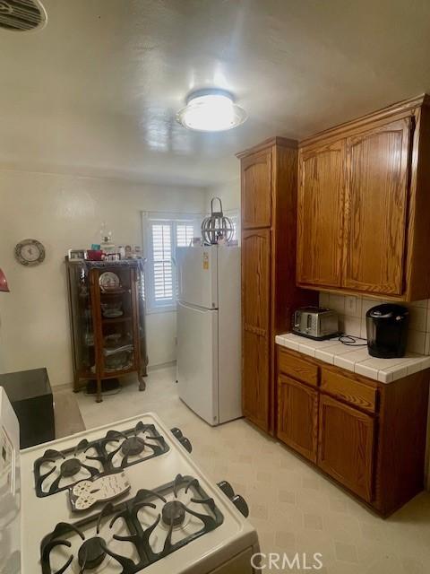 15343 Leahy Ave, Bellflower, CA 90706 - kitchen with white appliances, tile counters, brown cabinets, light floors, and backsplash