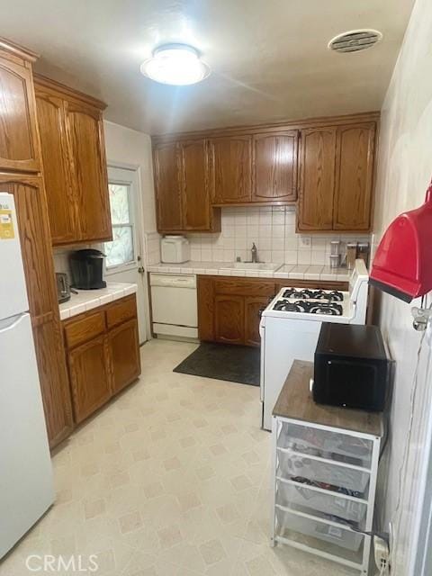 15343 Leahy Ave, Bellflower, CA 90706 - kitchen with white appliances, tile counters, brown cabinets, tasteful backsplash, and light flooring