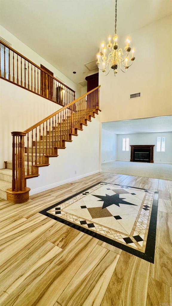 15696 Oakstand Rd, Poway, CA 92064 - unfurnished living room featuring stairway, a high ceiling, a chandelier, a glass covered fireplace, and wood finished floors
