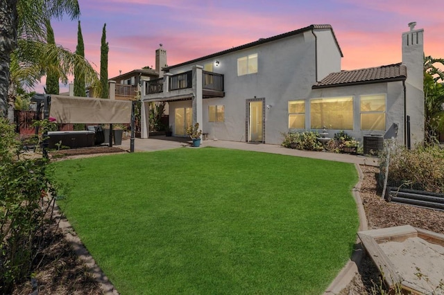 33740 Sattui St, Temecula, CA 92592 - back of property at dusk with a balcony, a covered hot tub, a patio area, a chimney, and a yard