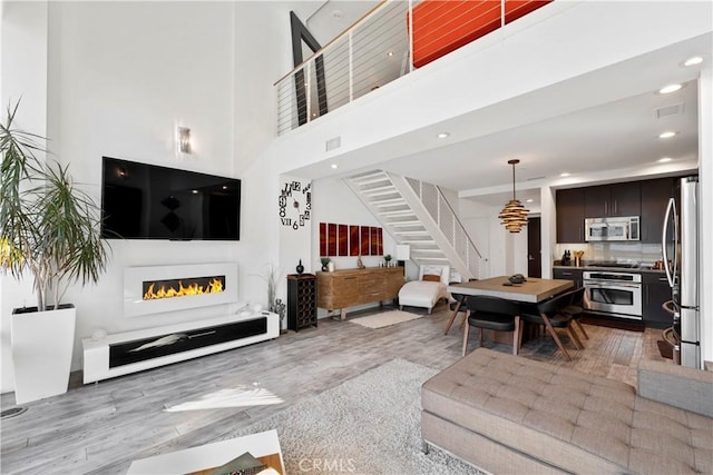 1100 Wilshire Blvd Unit 1707, Los Angeles, CA 90017 - living room featuring stairs, light wood-style flooring, a high ceiling, a warm lit fireplace, and recessed lighting