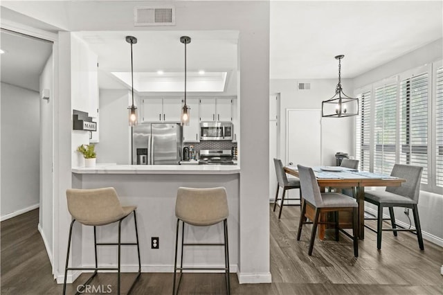 5722 E Stillwater Ave Unit 104, Orange, CA 92869 - kitchen featuring stainless steel appliances, white cabinetry, tasteful backsplash, a breakfast bar area, and dark wood finished floors