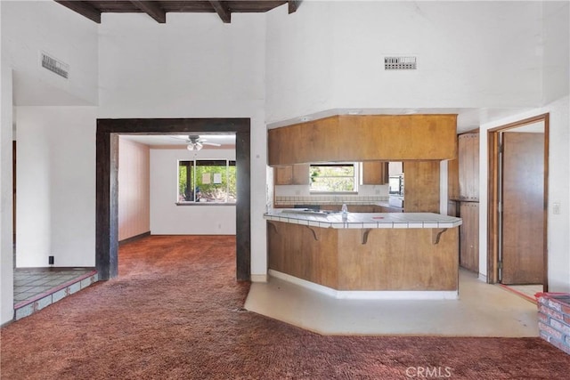 19215 Hupa Rd, Apple Valley, CA 92307 - kitchen featuring tile countertops, a high ceiling, light carpet, brown cabinetry, and a breakfast bar area