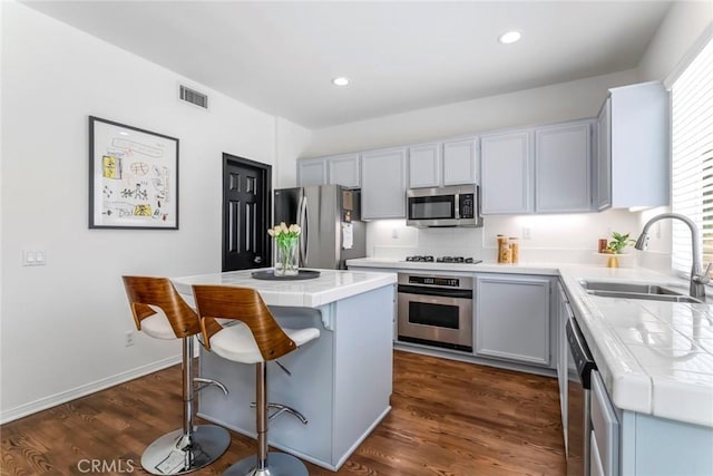 27960 Agapanthus Ln, Valencia, CA 91354 - kitchen featuring stainless steel appliances, a kitchen island, tile counters, a breakfast bar area, and dark wood-style flooring