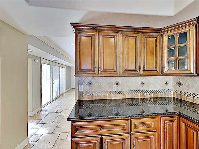 2030 Kingsbridge Way, Oxnard, CA 93035 - kitchen featuring decorative backsplash, brown cabinetry, stone tile flooring, dark stone countertops, and glass insert cabinets